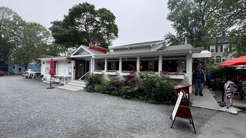 Quaint white cafe with a wraparound porch and outdoor seating on a gravel lot in Acadia National Park.