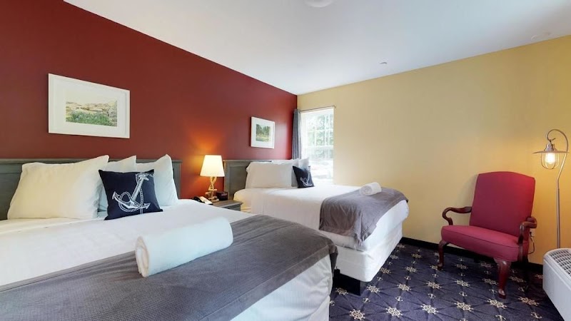 Two queen beds with white linens and gray throws, red accent wall, red chair and lamp in Acadia National Park.
