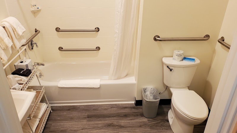 Bathroom with white tub and shower curtain, grab bars, toilet, towels and shelving in a lodge room at Acadia National Park