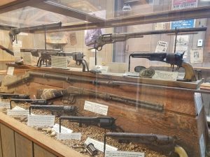 Historic firearms on display in a museum case at Cody Dug Up Gun Museum in Yellowstone National Park