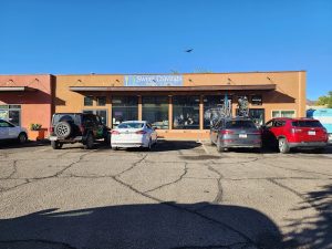 Arches National Park area storefront with a brown brick facade, a signboard, several parked cars, and a clear blue sky.
