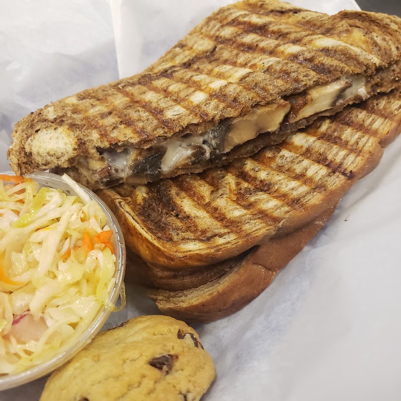 Grilled panini with melted cheese and a dark filling sits beside a creamy coleslaw cup and a cookie at Arches National Park.