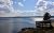 Shimmering Yellowstone Lake seen from a rocky shore with a wooden boardwalk, a lone pine, and a bright, cloudy sky.
