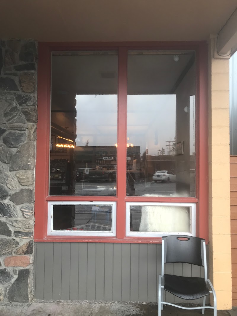 Yellowstone National Park storefront with red window frames, stone wall left, a chair outside, reflections of street traffic