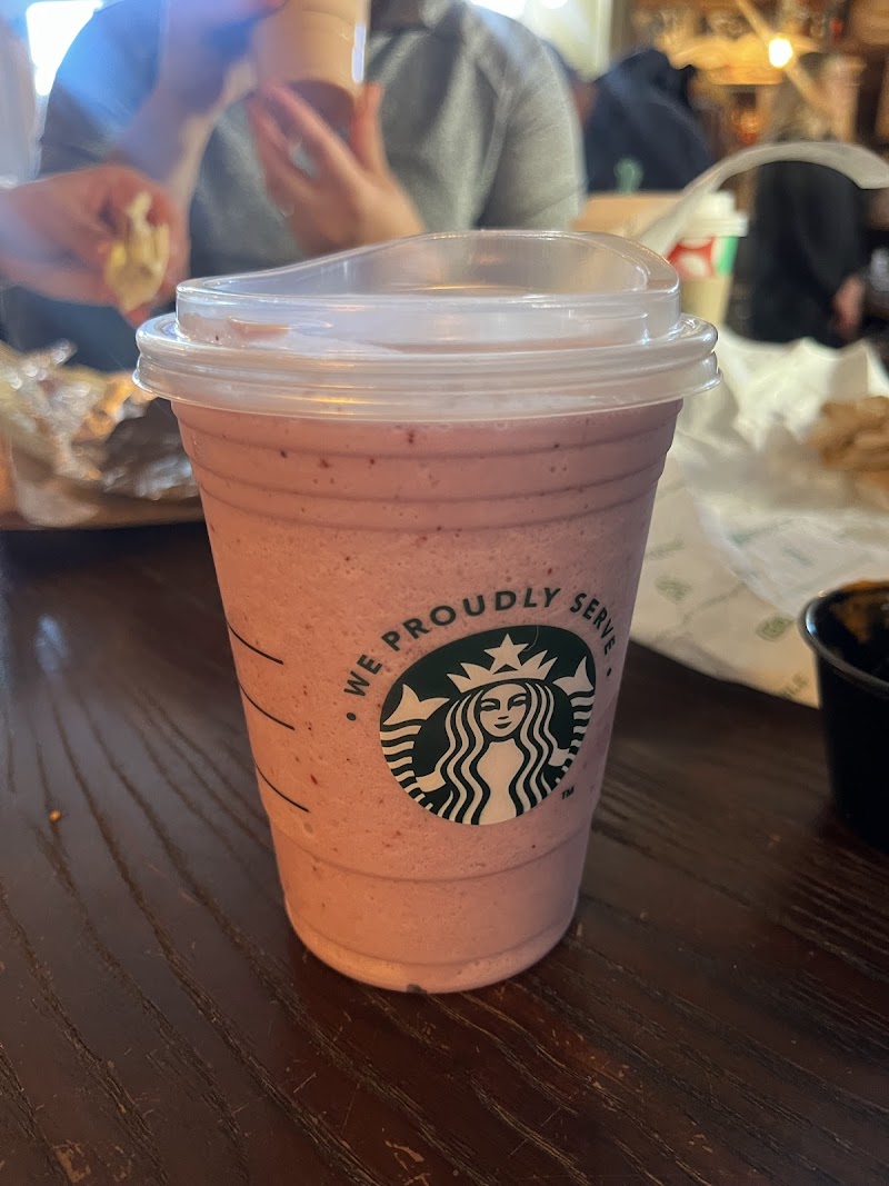 Pink strawberry smoothie in a clear cup on a dark wood table at Yellowstone National Park, with blurred diners in background.