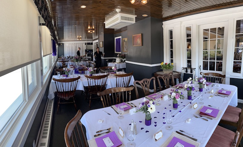 Dining room interior at a lodging facility in Acadia National Park, with long white-tablecloth tables, purple napkins and floral centerpieces.