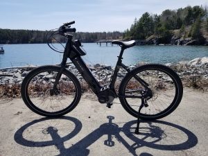 Electric bike parked on a sandy path beside a rocky shore, calm water and a wooden dock in Acadia National Park.