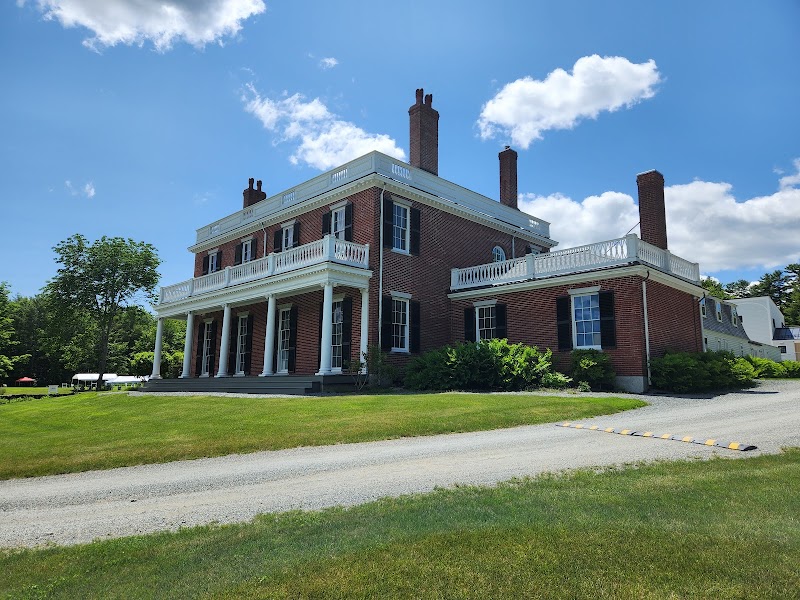 The Black House Museum at Woodlawn, brick Georgian-style house with white columns, sits on a green lawn in Acadia National Park.