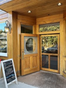 Wood-toned storefront entrance with double doors, glass panels, a chalkboard sign, and vintage lantern lighting in Acadia National Park.