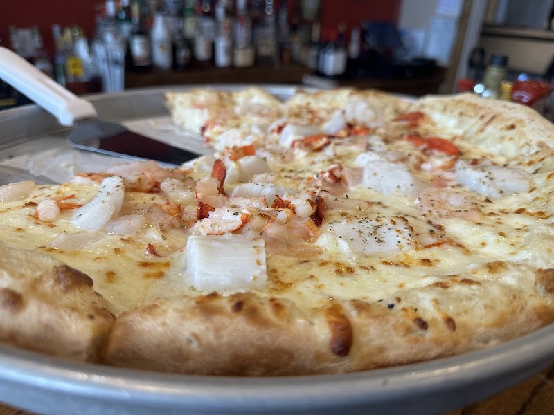 Lobster and onion cheese pizza on a metal pan, with a bar backdrop at Acadia National Park.