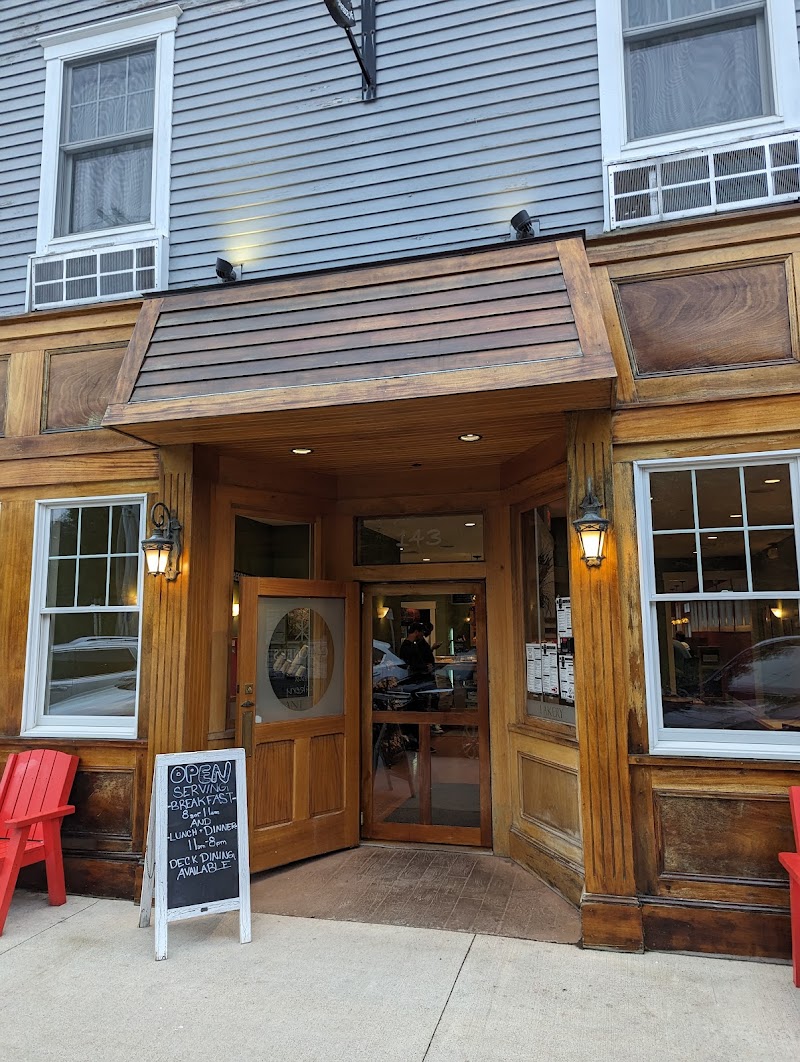 Wooden storefront with open door, chalkboard menu, red chairs, and warm lamps at a rustic cafe in Acadia National Park.