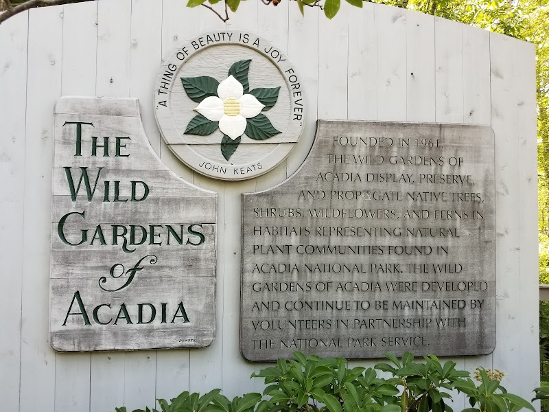 The Wild Gardens of Acadia sign at Acadia National Park with a circular floral emblem and park history plaque.