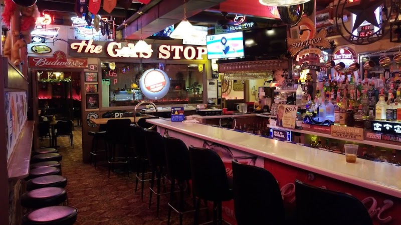Neon-lit bar interior with a long counter, black stools, and eclectic signs in Badlands National Park area.