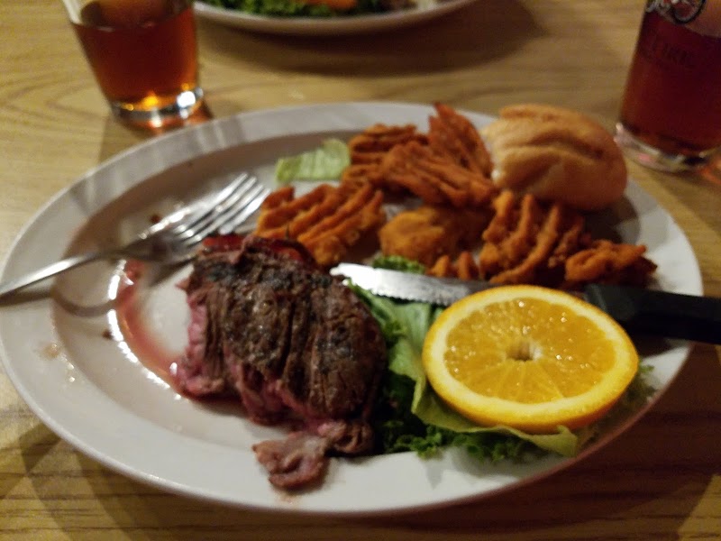 Sliced steak on greens with an orange wedge, crinkle fries, a roll, and drinks on a table at Badlands National Park.