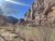 Arches National Park scene with a calm river beside towering red rock cliffs and leafless shrubs along a dirt trail.
