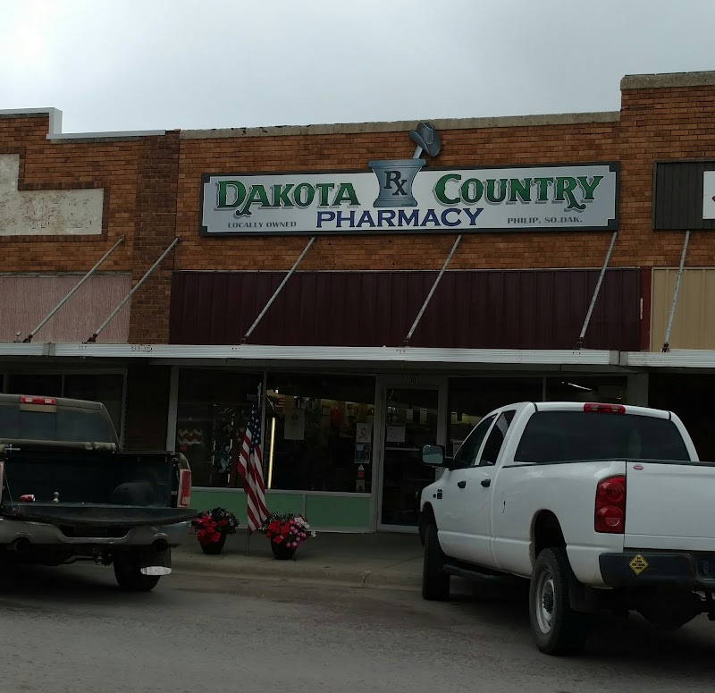 Philip, Badlands National Park: brick storefront, green and blue sign, two pickup trucks out front, and potted flowers.