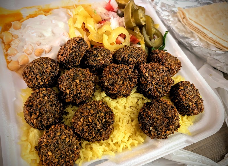 In a takeout foam box in Yellowstone National Park, falafel balls rest on yellow rice with pickles and yogurt sauce.