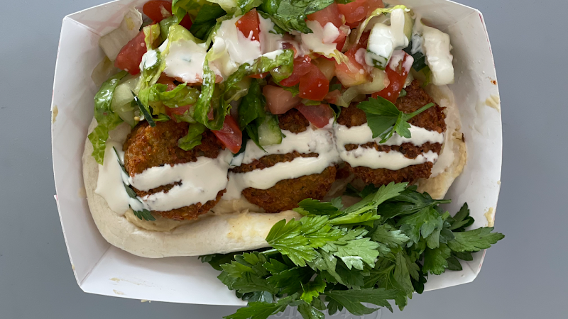 Falafel patties with white sauce, tomatoes, cucumbers, greens, and parsley in a pita, in a takeout box—Yellowstone National Park.