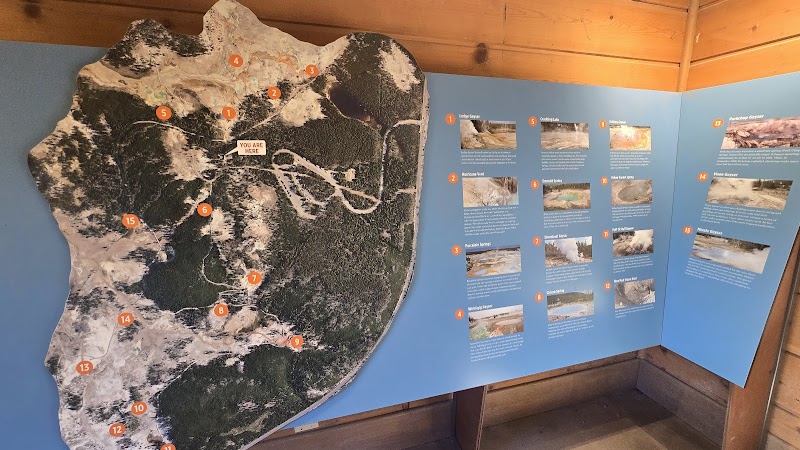 Large map of the area with orange numbered markers on a blue wall beside information panels inside Yellowstone National Park.