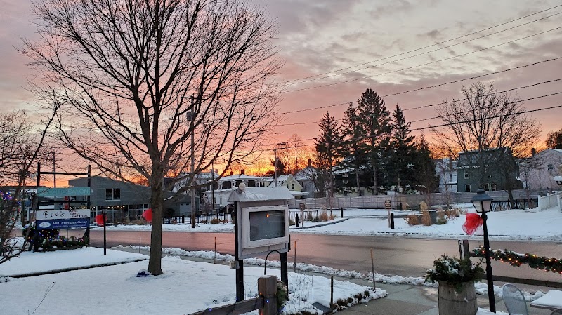 Bar Harbor town center in Acadia National Park at sunset, wintery street with snow-covered sidewalks and parked cars.