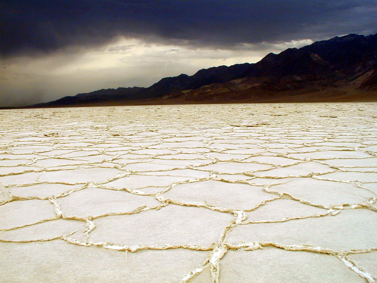 Cracked white salt flats of Badwater Basin stretch toward distant mountains in Death Valley National Park.
