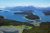 Aerial view over Glacier Bay National Park & Preserve with forested islands, inlets, and snow‑capped mountains under a blue sky.