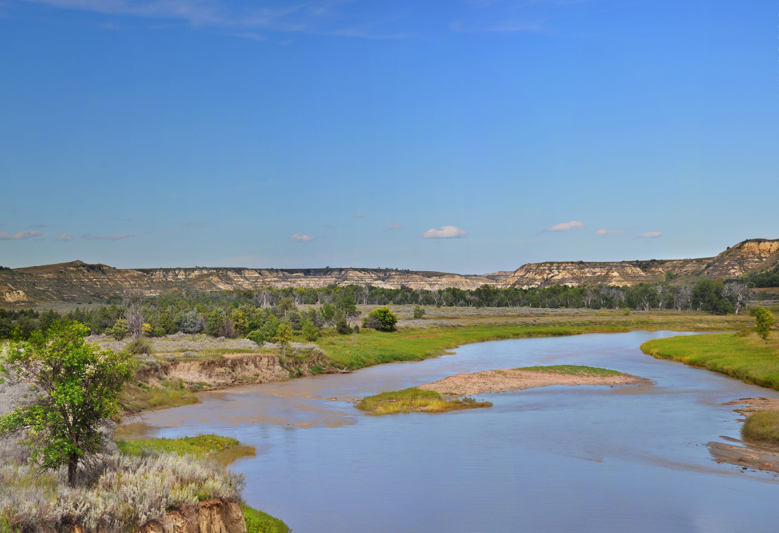 The Little Missouri River winds through Theodore Roosevelt National Park's badlands under a clear blue sky.