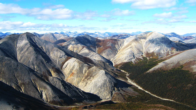 Snowy gray mountain ridges rise above a winding valley in Kobuk Valley National Park, Alaska, under a bright blue sky.