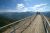 Visitors stand on a paved, railing-lined viewing platform on Moro Rock, Sequoia & Kings Canyon National Parks, with Sierra Nevada peaks and a blue sky.
