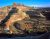 Panoramic view from an Island in the Sky overlook in Canyonlands National Park, showing red and tan layered sandstone fins and distant buttes under a bright blue sky.
