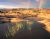 Sunlit red sandstone slickrock with water-filled pools and a double rainbow over Canyonlands National Park.
