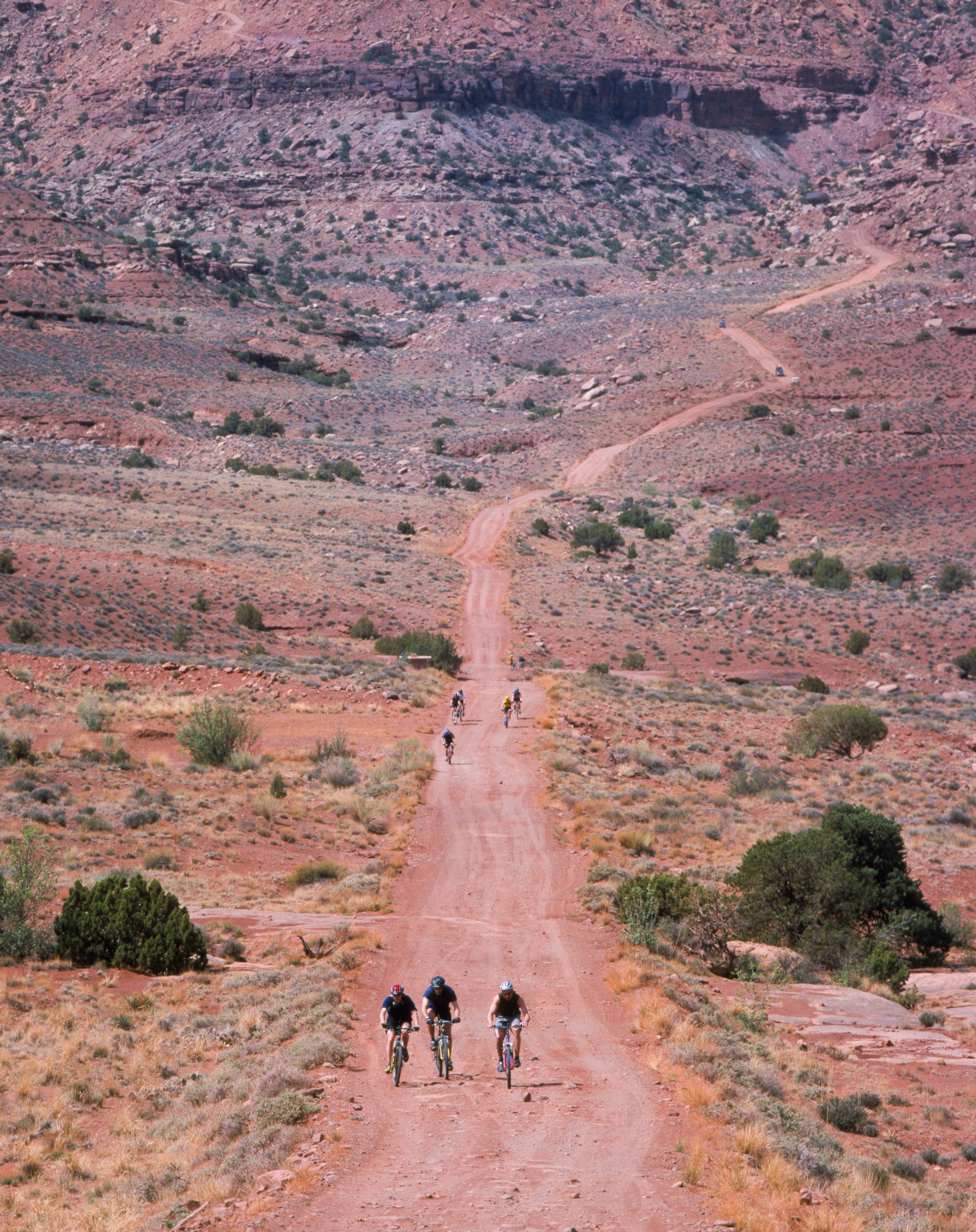 Island in the Sky backcountry road winds through red canyon terrain in Canyonlands National Park, with distant riders on a dusty route.
