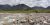 Two hikers cross a rocky riverbank with glacial mountains rising behind in Gates of the Arctic National Park & Preserve.