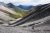 Two hikers descend a gray scree slope above a green valley in Gates of the Arctic National Park & Preserve, Alaska, with jagged mountain peaks in the distance.