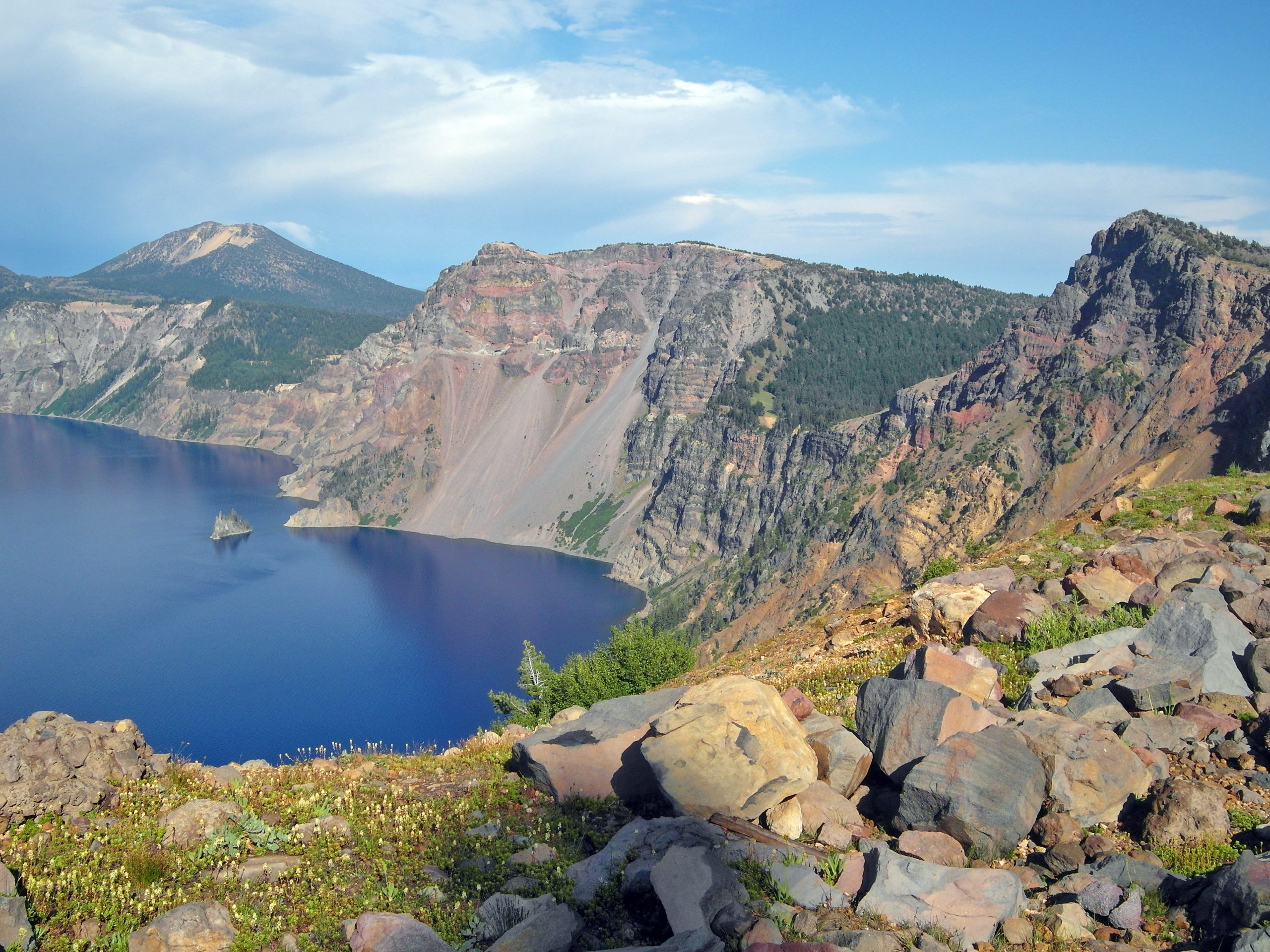 Crater Lake National Park rim overlook view with deep blue lake and rugged caldera walls in sunlight.