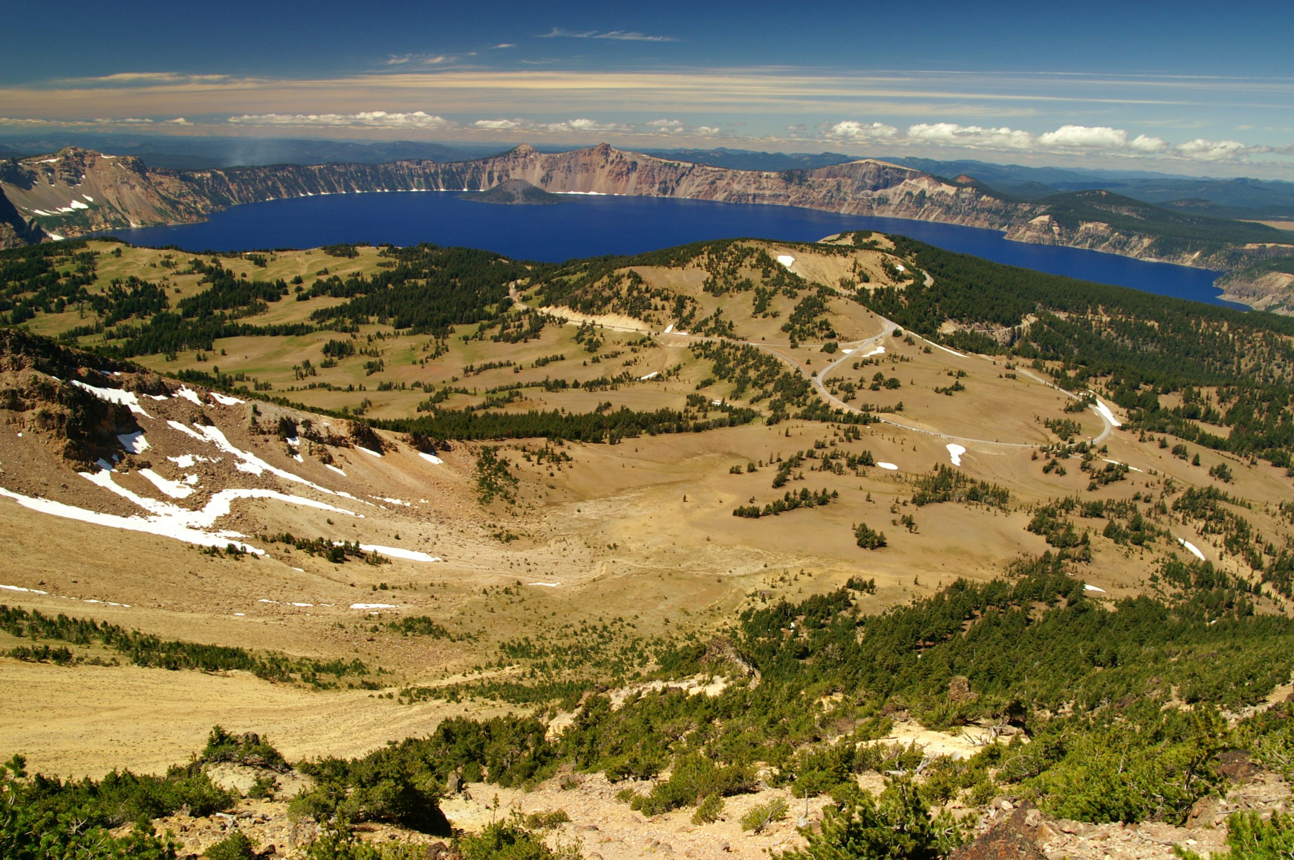 Crater Lake National Park crater rim overlook showing the deep blue caldera lake with surrounding cliffs and grassy slopes.