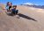 Three kids ride a sandy dune at Great Sand Dunes National Park & Preserve, with snow-capped mountains rising in the distance against a clear blue sky.
