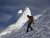 Climber in a yellow jacket and red helmet ascends a snowy slope with a jagged icy peak in Mount Rainier National Park.