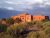 Painted Desert Inn, a red adobe structure in Petrified Forest National Park, surrounded by desert shrubs under a dramatic sky.