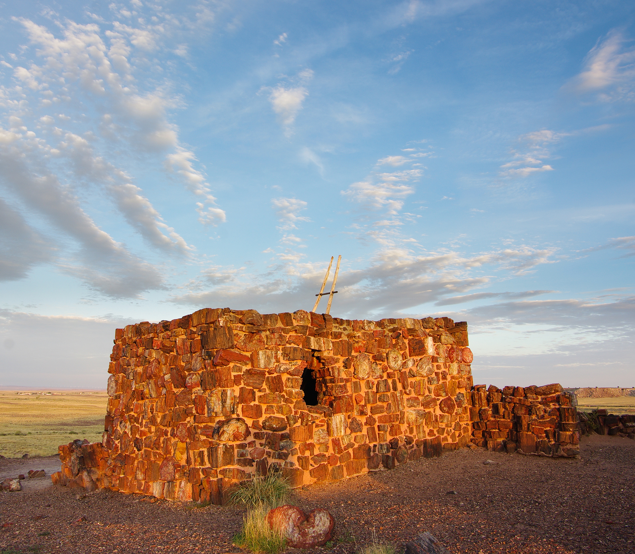 Painted Desert Inn Ruins rise from the desert in Petrified Forest National Park at sunset with a stone wall and sparse grass.
