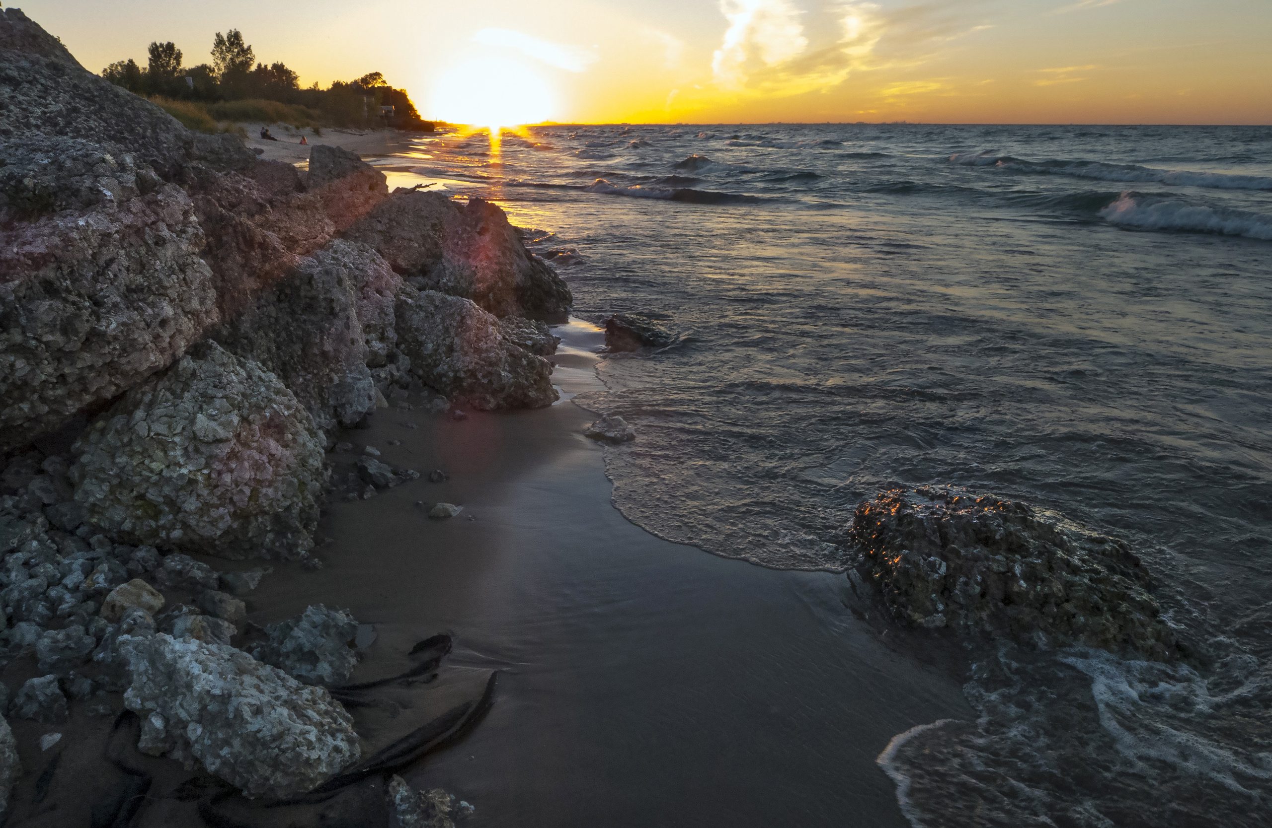 Sunset over the rocky shoreline at Indiana Dunes National Park, with waves washing the sandy beach along Lake Michigan.