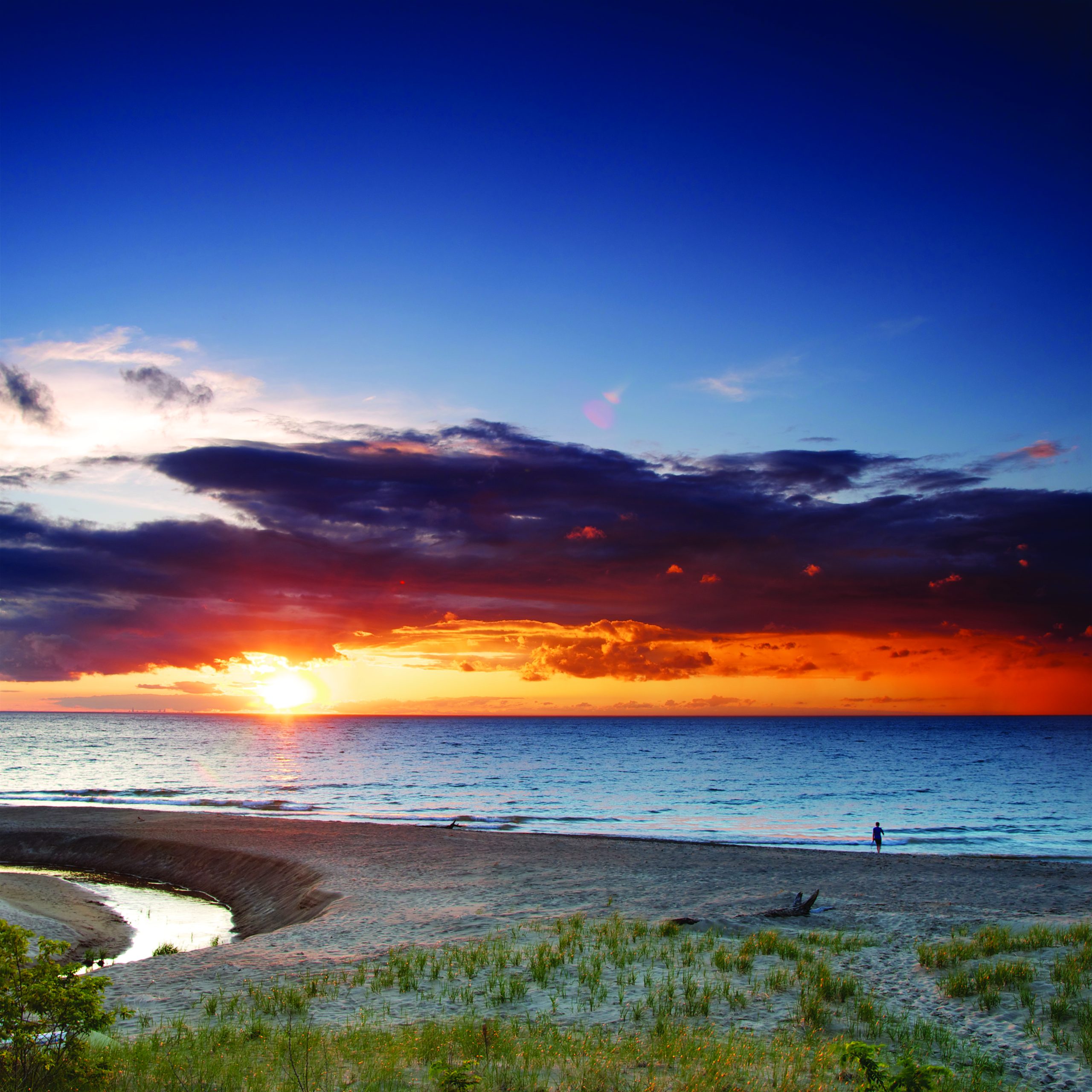 Sunset over Lake Michigan at Indiana Dunes National Park, with a warm orange horizon and a lone figure on the beach.