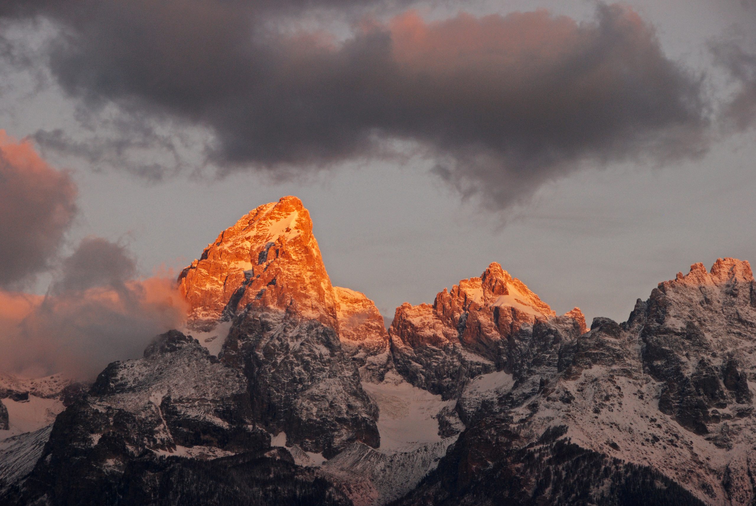Grand Teton rises with a warm sunset glow over snow-dusted peaks in Grand Teton National Park.