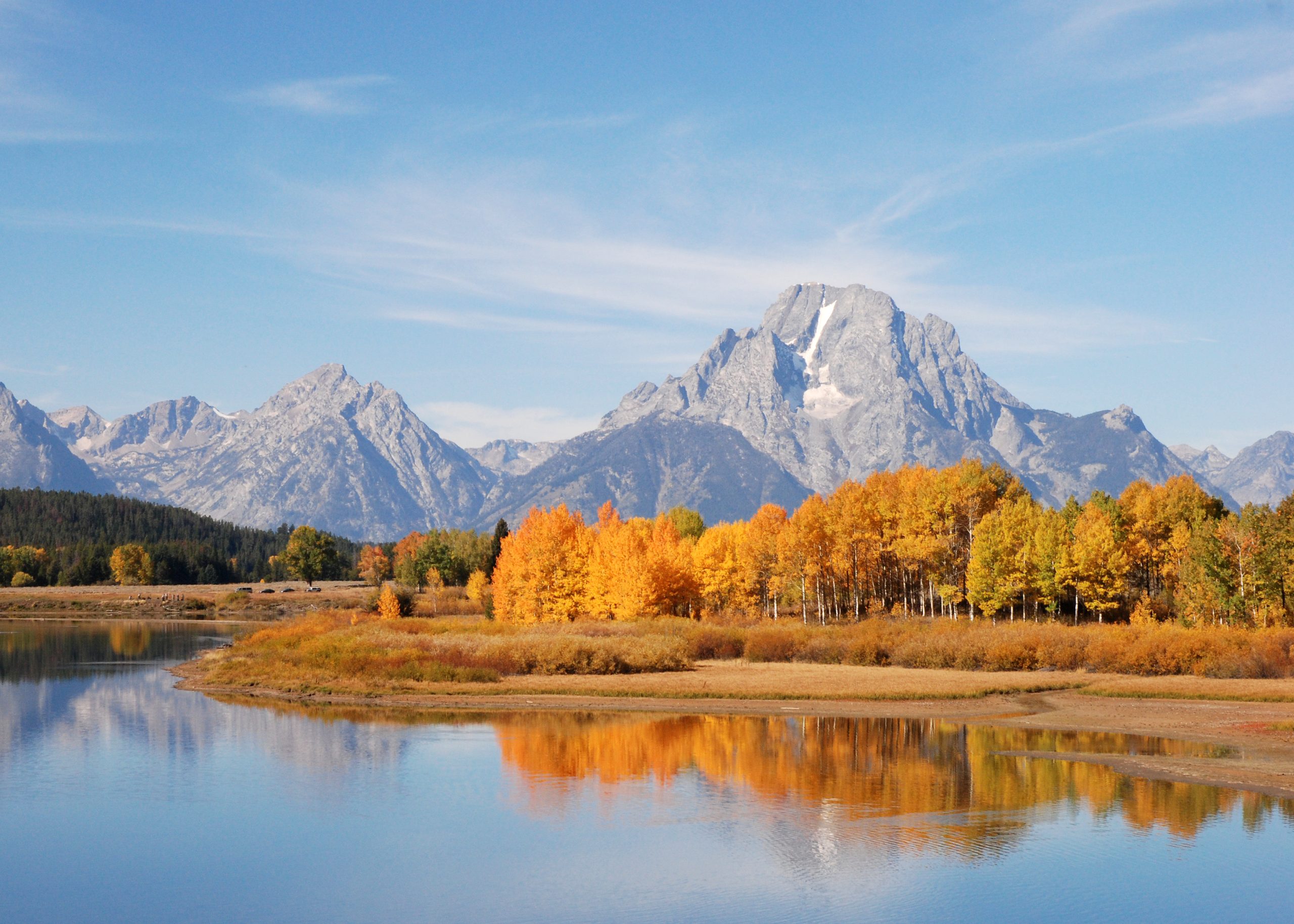 Oxbow Bend overlook in Grand Teton National Park frames the Grand Teton with autumnal orange trees and a calm reflective lake.