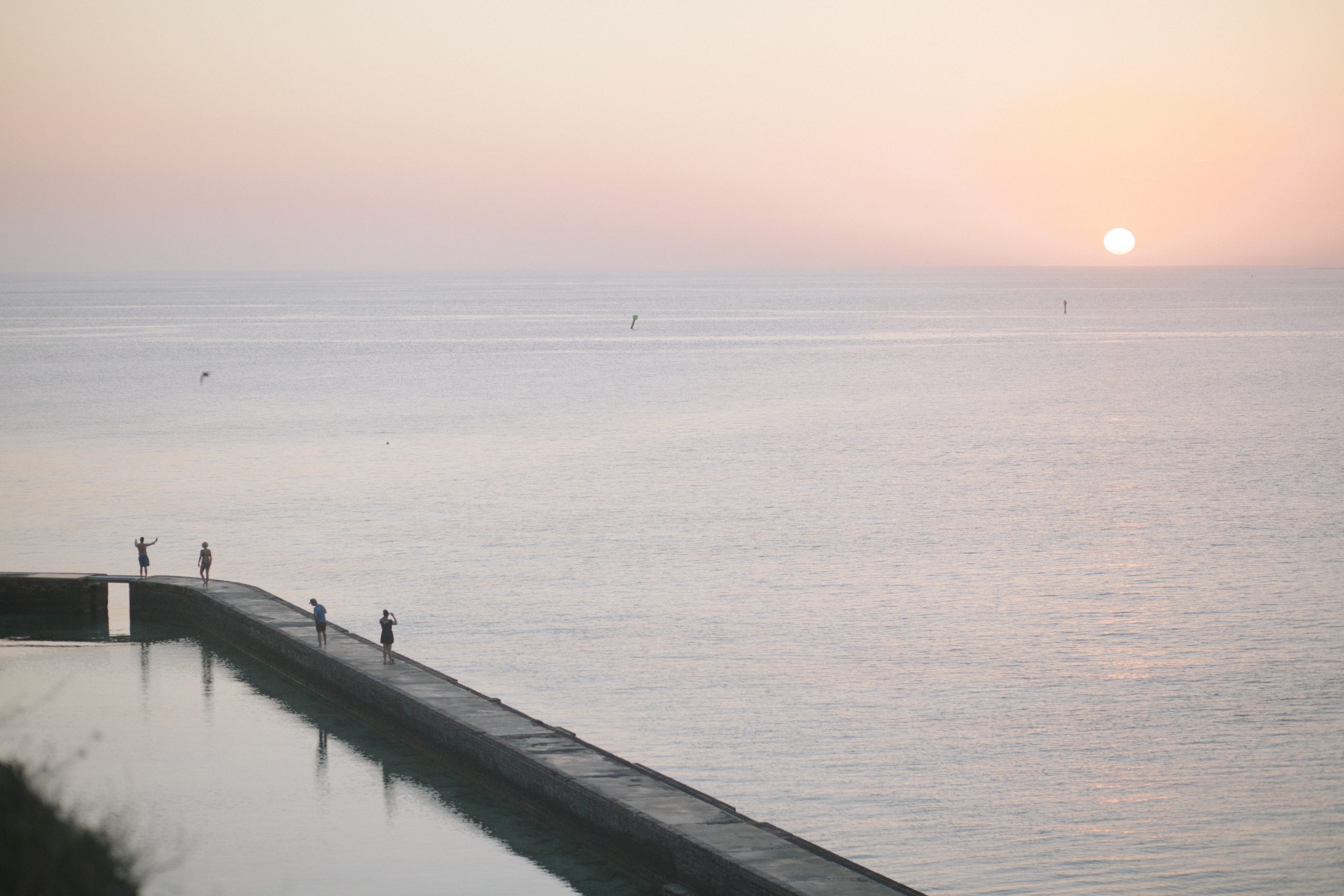 Sunset over calm Gulf waters along the Dry Tortugas National Park Fort Jefferson jetty, with a few people standing at the edge.