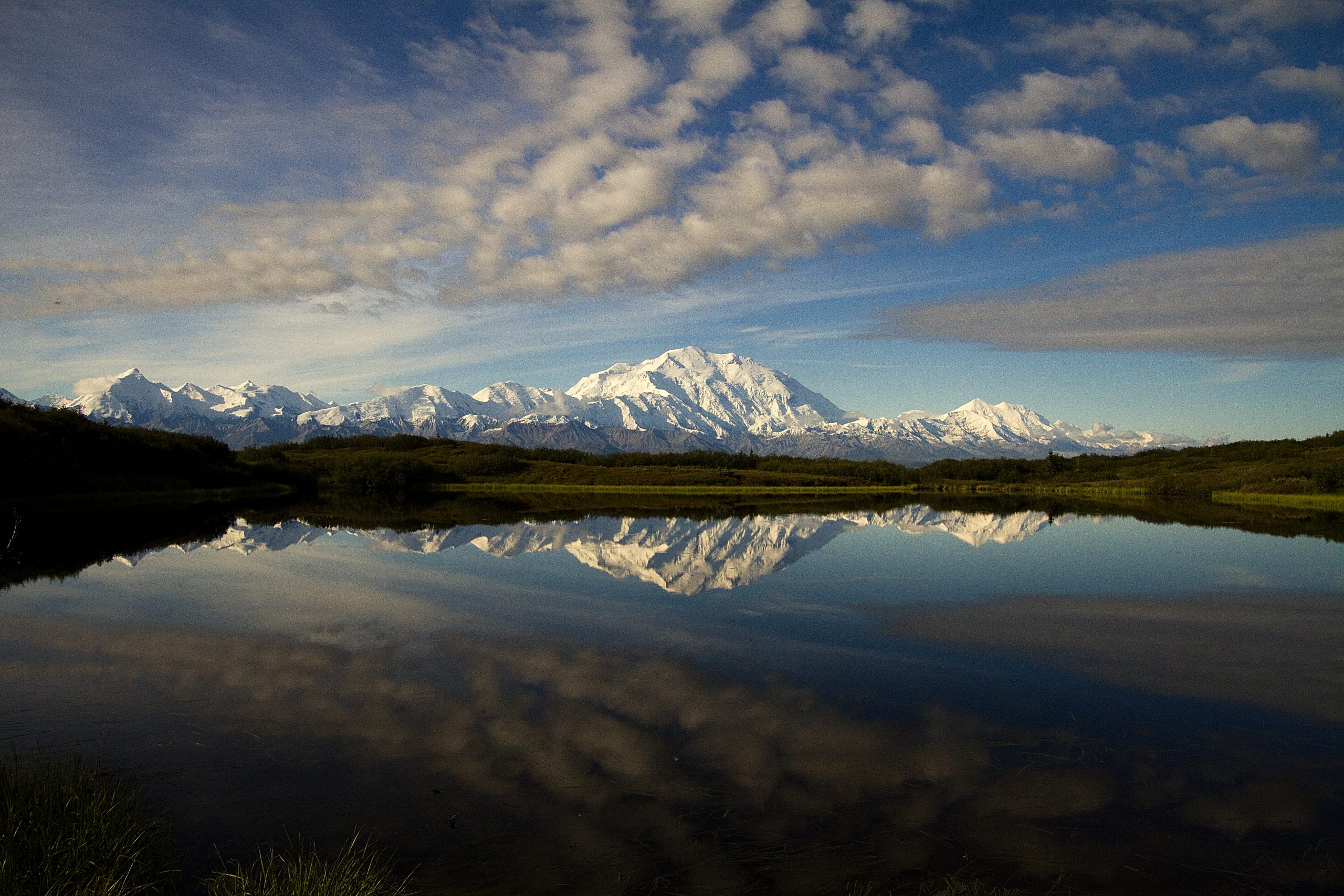 Snowy Denali rises behind Wonder Lake with a glassy foreground reflecting the mountain and sky.