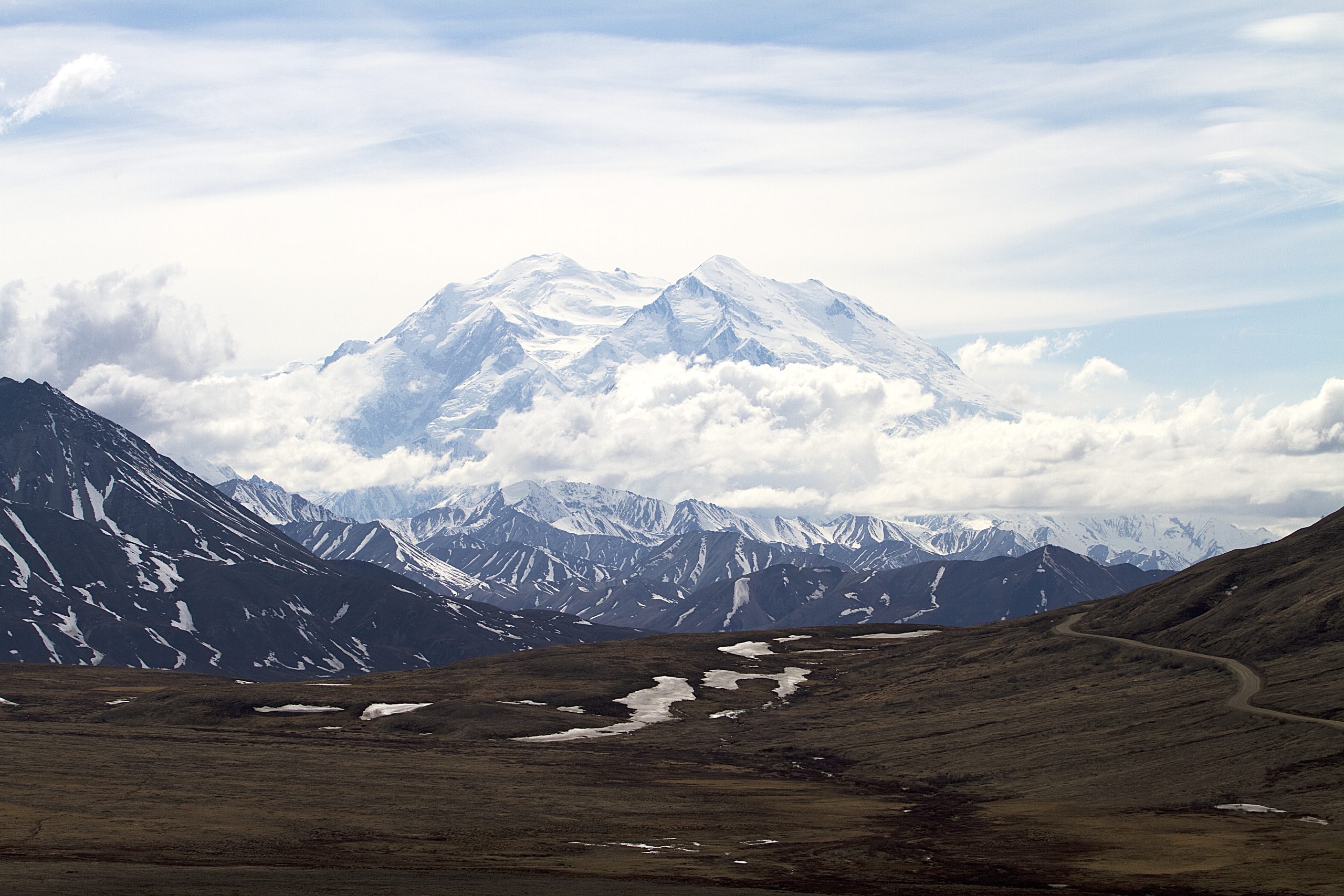 A snow-capped Denali peaks over rugged ridges viewed from a distant overlook in Denali National Park & Preserve.