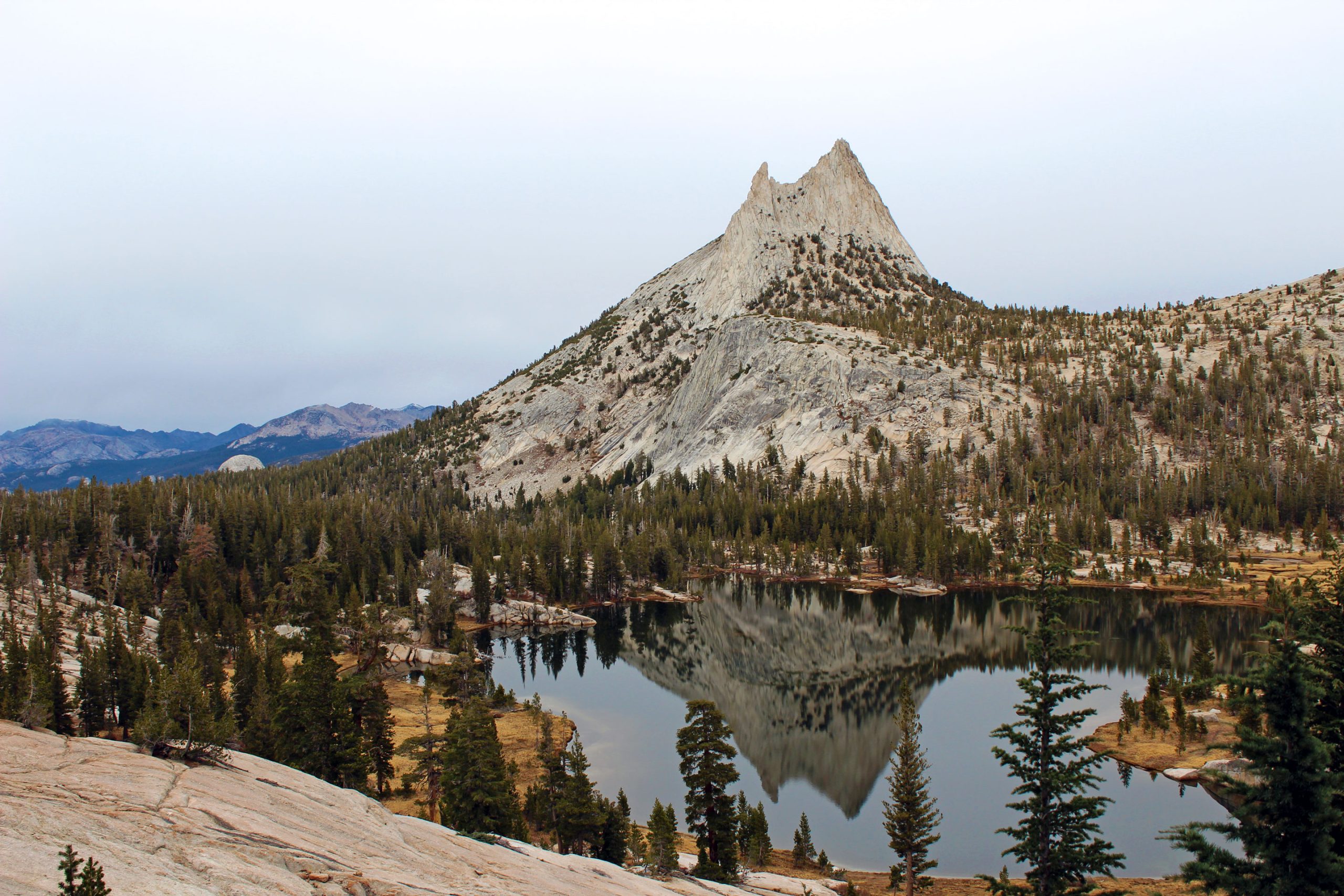 Cathedral Peak towers above Cathedral Lakes with a forested slope and a mirror-like alpine lake in Yosemite National Park.