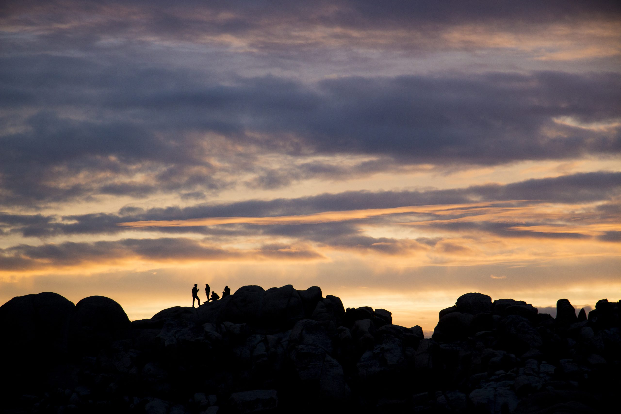 Sunset silhouettes stand atop rugged boulders at Hidden Valley in Joshua Tree National Park.