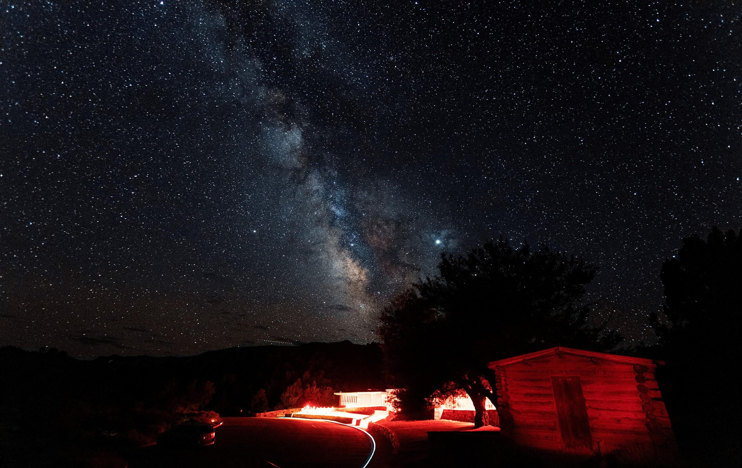 Night sky over Wheeler Peak Lodge at Great Basin National Park, with a red-lit lodge exterior along a winding road.